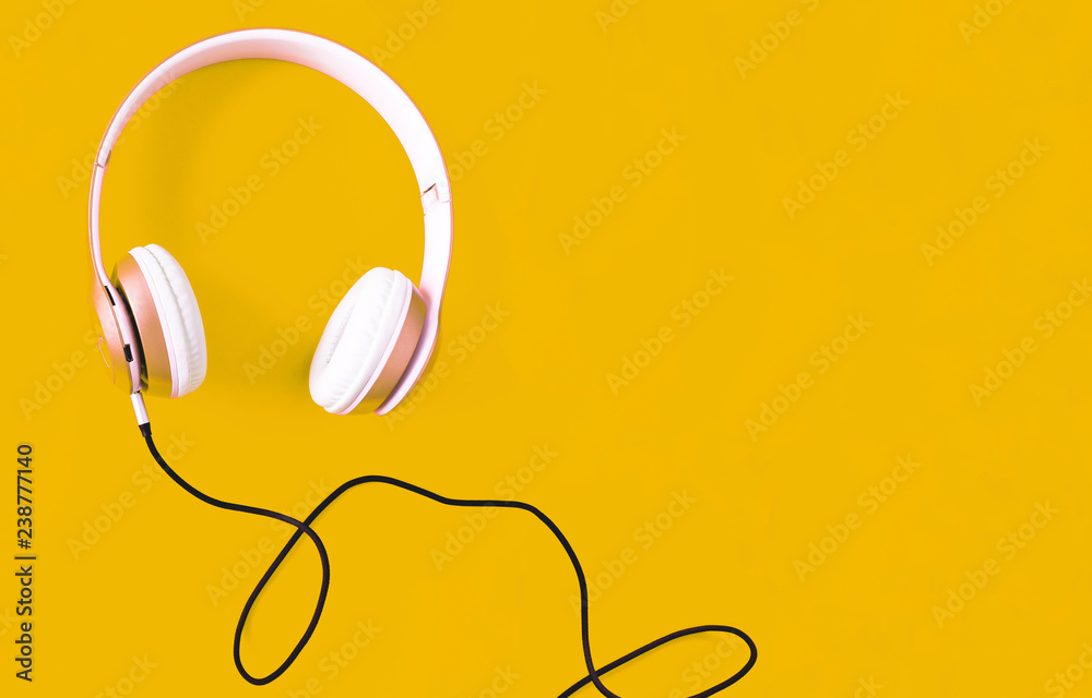 Pink headphone and black cable on pastel color yellow background. Music concept. Blank copy space Pink headphone and black cable on pastel color yellow background. Music concept. Blank copy space