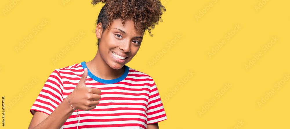Beautiful young african american woman over isolated background doing happy thumbs up gesture with hand. Approving expression looking at the camera showing success. Beautiful young african american woman over isolated background doing happy thumbs up gesture with hand. Approving expression looking at the camera showing success.