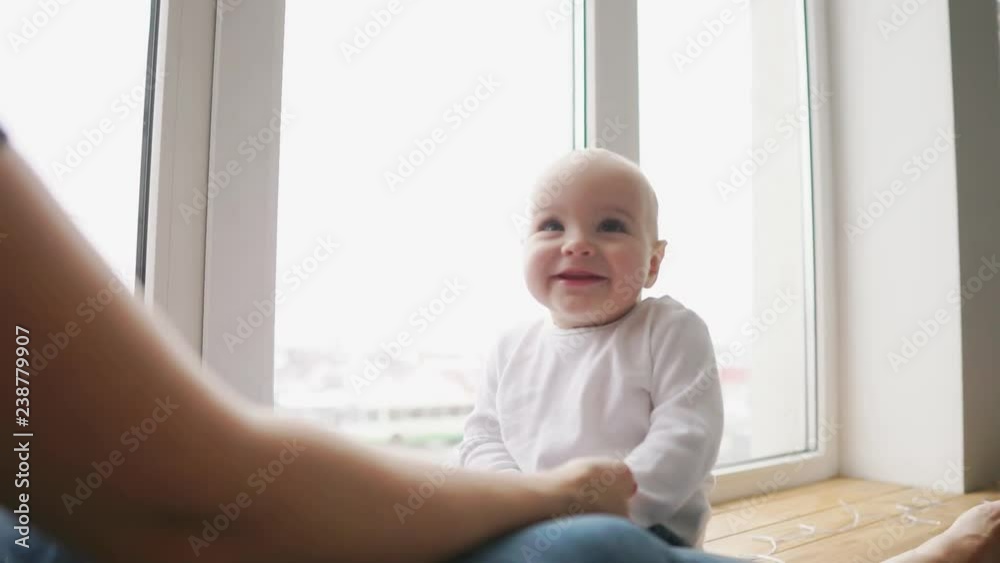 Mother and her baby son having fun and playing at home. Little kid 1 years old play with his mom arms at home near a big window Mother and her baby son having fun and playing at home. Little kid 1 years old play with his mom arms at home near a big window