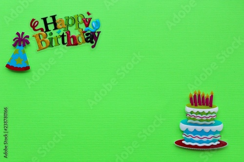 happy birthday written in upper left corner with a birthday cake with candle in the bottom right corner on a green background with writing space