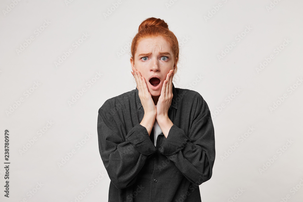 Amazed frowning female shocked and touching cheeks. Astonished girl not believing her eyes. Photo of young woman with stunned expression, dressed casually, poses against white background. Amazed frowning female shocked and touching cheeks. Astonished girl not believing her eyes. Photo of young woman with stunned expression, dressed casually, poses against white background.
