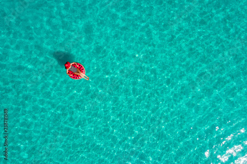 Aerial view of slim woman swimming on the swim ring  donut in the transparent turquoise sea in Seychelles. Summer seascape with girl  beautiful waves  colorful water. Top view from drone