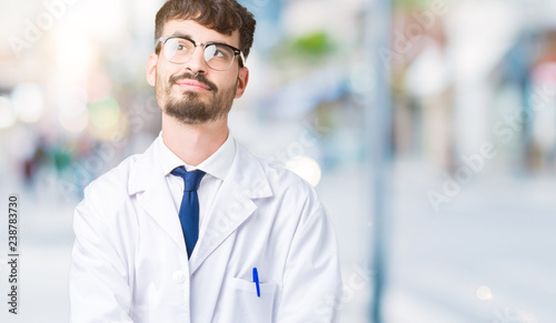 Young professional scientist man wearing white coat over isolated background smiling looking side and staring away thinking.