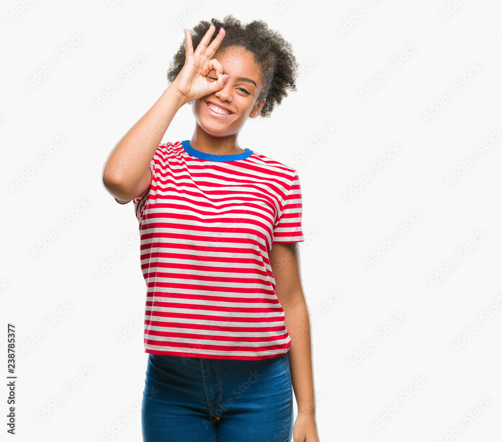 Young afro american woman over isolated background doing ok gesture with hand smiling, eye looking through fingers with happy face. Young afro american woman over isolated background doing ok gesture with hand smiling, eye looking through fingers with happy face.