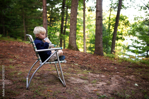 Cute Little Kid Sipping Juice While Sitting in a Lawn Chair at a Campground Overlooking a Lake