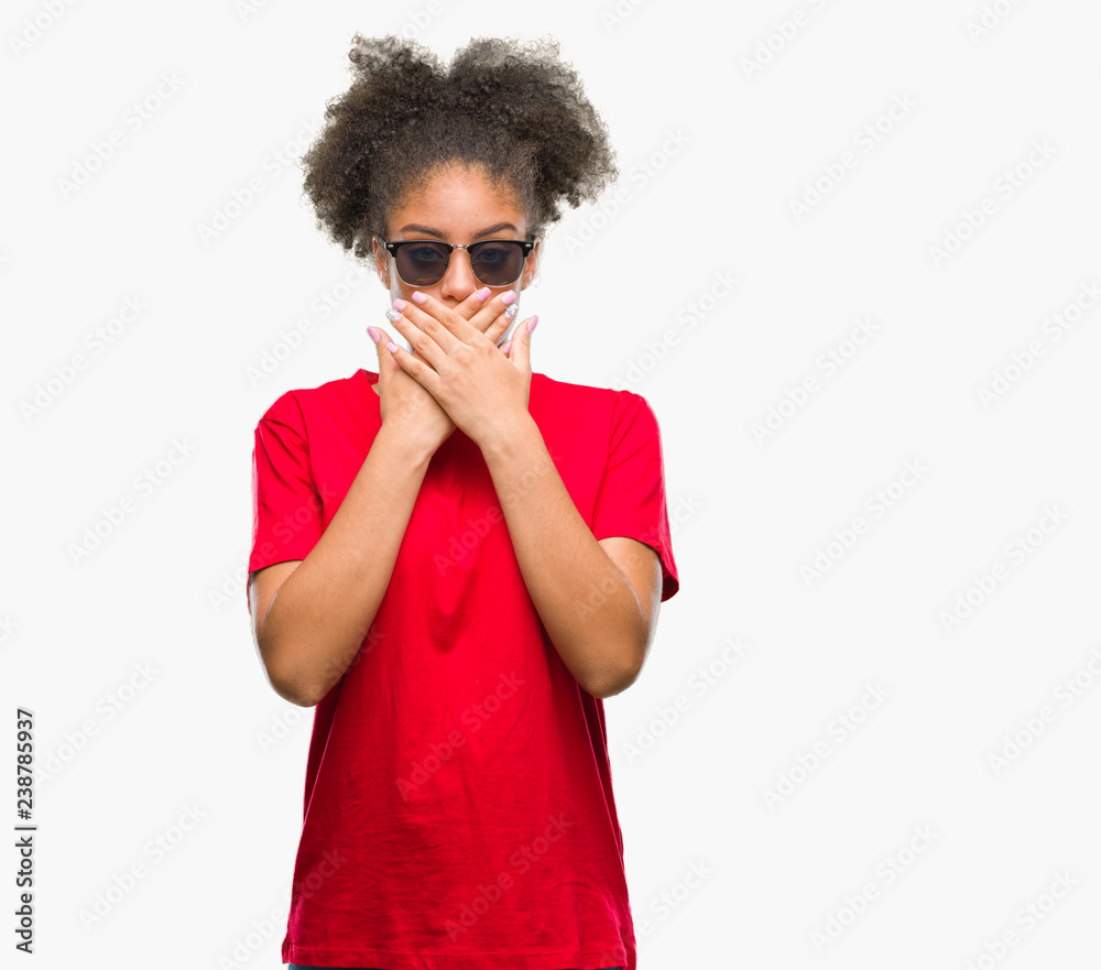 Young afro american woman wearing sunglasses over isolated background shocked covering mouth with hands for mistake. Secret concept. Young afro american woman wearing sunglasses over isolated background shocked covering mouth with hands for mistake. Secret concept.