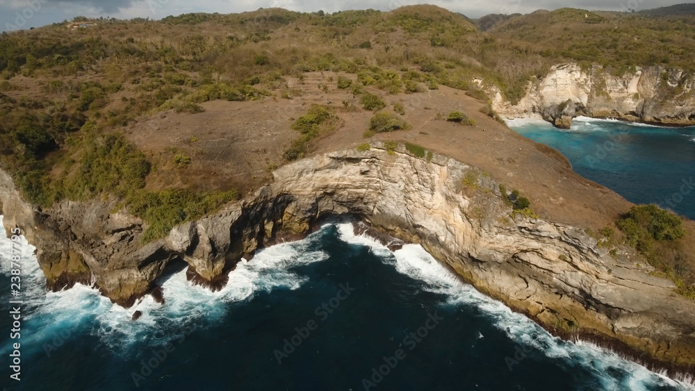 Aerial view of Rocky coast with high cliffs, sea surf with breaking waves on the coast, Nusa Penida, Bali, Indonesia. Ocean with waves and rocky cliff. Travel concept