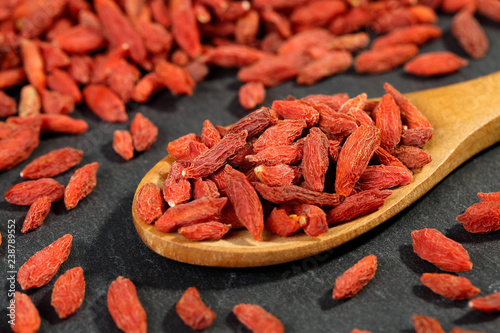 Extreme close up of dried organic goji berry fruits (wolfberries) in a wooden spoon on a black stone surface. Selective focus and shallow depth of field