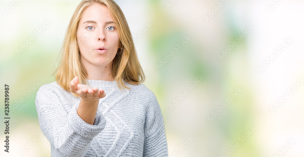 Beautiful young woman wearing winter sweater over isolated background looking at the camera blowing a kiss with hand on air being lovely and sexy. Love expression.