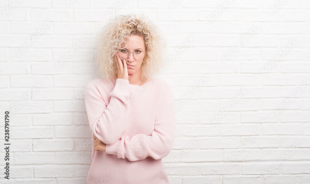 Young blonde woman with curly hair over white brick wall thinking looking tired and bored with depression problems with crossed arms. Young blonde woman with curly hair over white brick wall thinking looking tired and bored with depression problems with crossed arms.