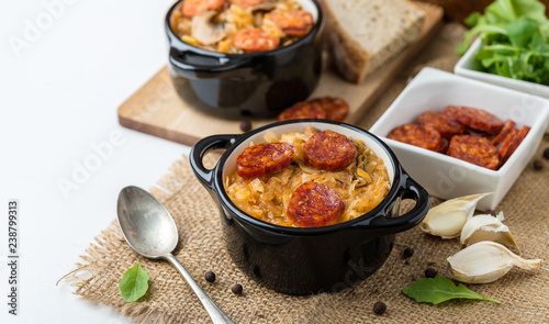 Slovak Christmas national cabbage soup in two small black pots with sausage on the jute background.