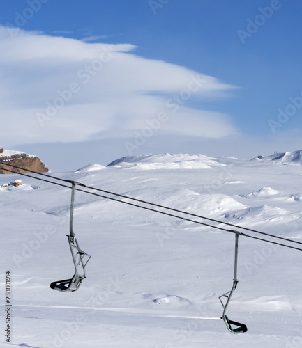 Snowy slope, chair-lift and blue sky with clouds at sunny winter day