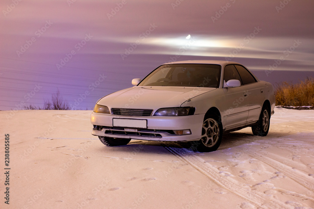 white sports car in the snow at night with a full moon in the clouds