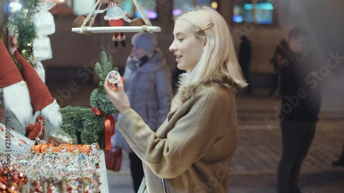 Young blonde girl having fun at christmas market in a city. Happy attractive woman in a christmas market at night. Beautiful bokeh lights background.