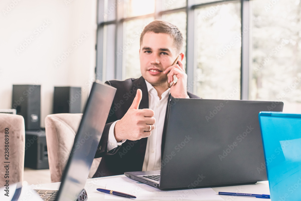 Businessman showing thumbs up while using laptop in office Businessman showing thumbs up while using laptop in office