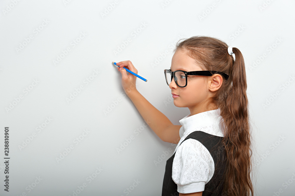 Smart pupil kid girl in eyeglasses looking on the wall background with drawing pencil Smart pupil kid girl in eyeglasses looking on the wall background with drawing pencil