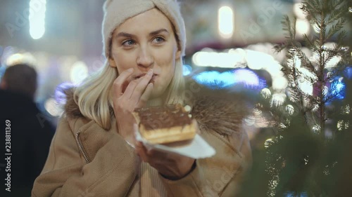 Happy attractive woman eating waffle with chocolate in a christmas market at night. Beautiful bokeh lights background.