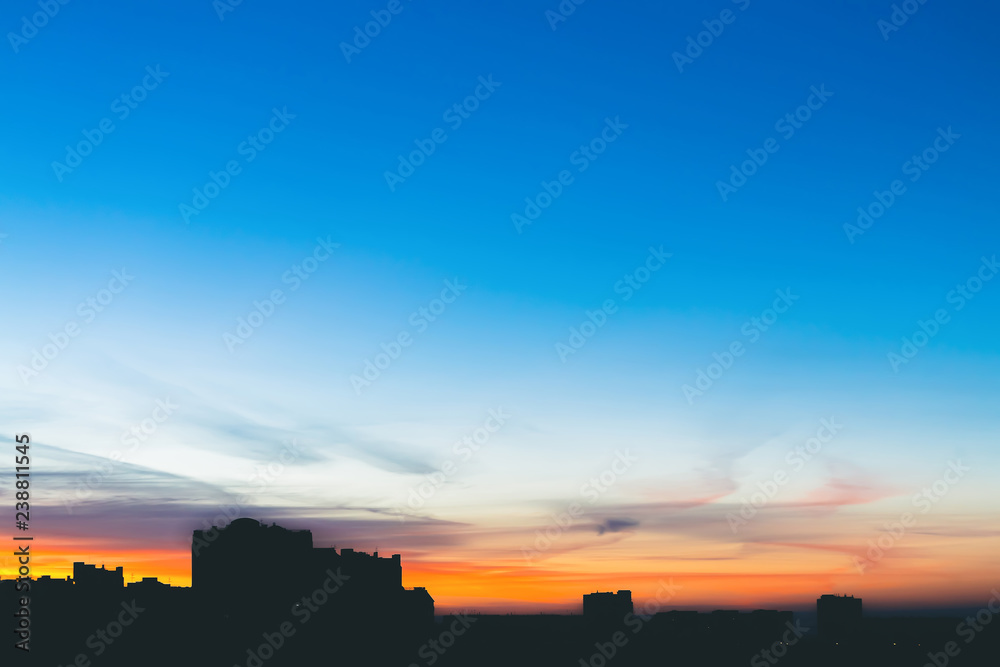 Cityscape with wonderful varicolored vivid dawn. Amazing dramatic blue sky with purple and violet clouds above dark silhouettes of city buildings. Atmospheric background of orange sunrise. Copy space.