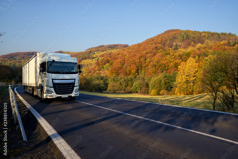 White truck driving on asphalt road around the mountain with deciduous trees in autumn colors