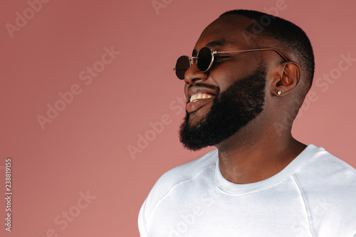 Man portrait. Style. Handsome Afro American guy in white T-shirt and sun glasses is smiling, on a pink background