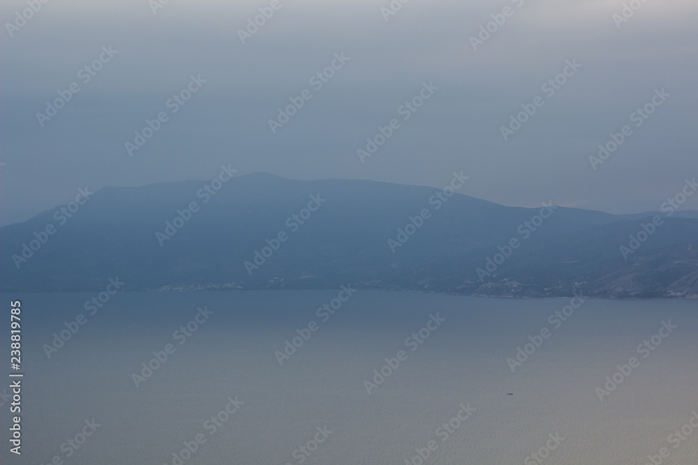 abstract nature landscape wallpaper background pattern of mountain ridge unfocused silhouette on big lake with calm water surface shore line in morning cloudy and foggy weather time