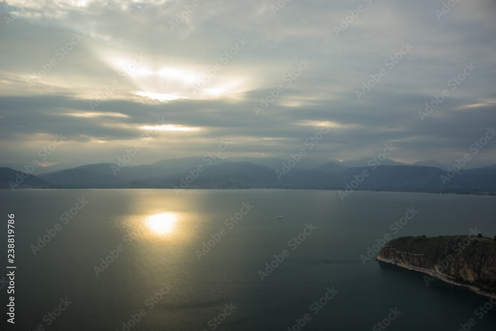 morning sun rise time and cloudy rainy foggy weather time in aerial shot with calm sea bay water surface with reflection, cape on shore line and mountain range horizon background landscape 
