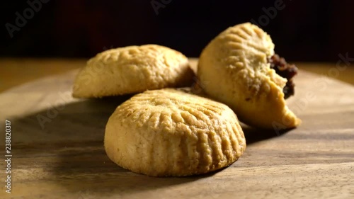 Three maamoul, arabic cookies with one broken open to see the date filling, rotating slowly in pretty light with black background. photo