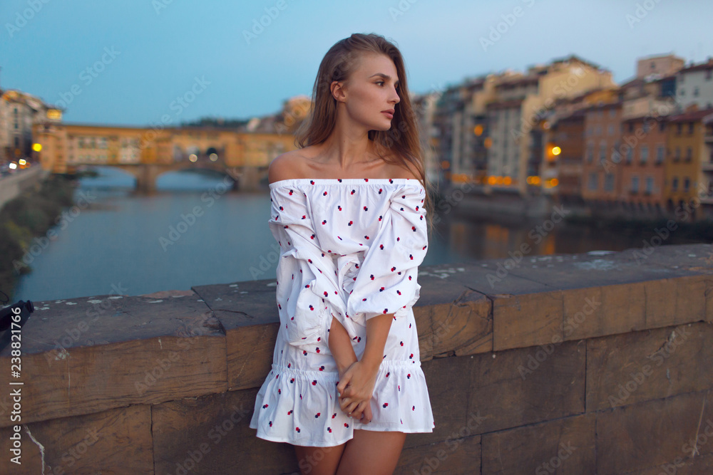 Beautiful girl in a white dress in the evening on the bridge in the city of Florence
