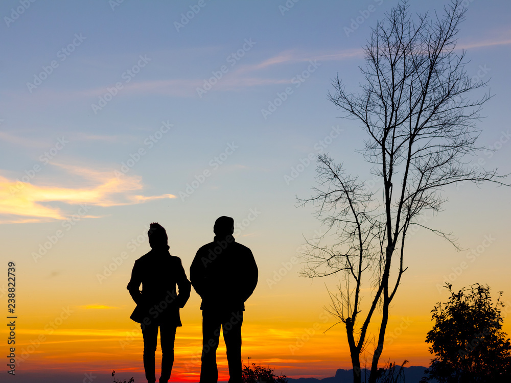 Silhouette of happy couple standing on the mountain at the sunset or sunrise time.