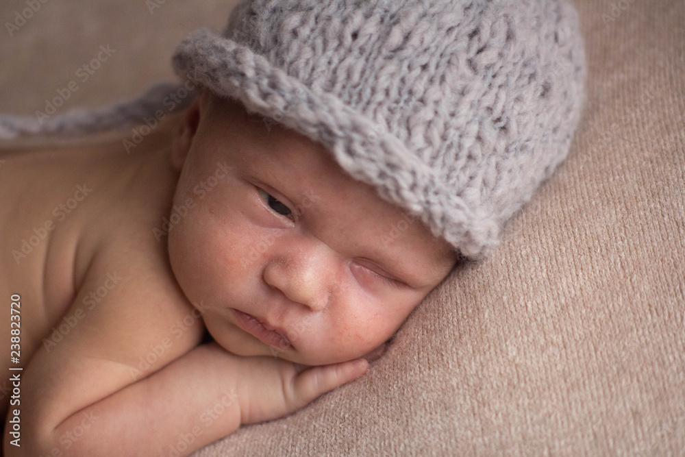 the first photo shoot. newborn child. the kid in the gray hat. the child lies on a beige blanket