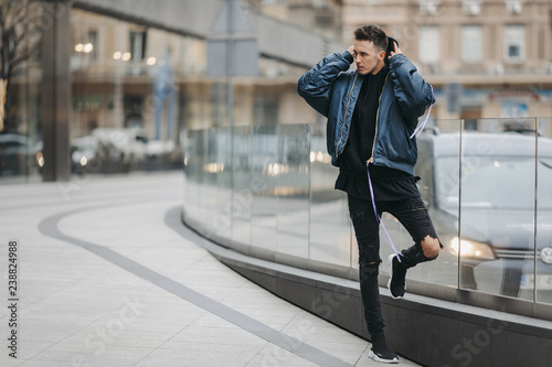 Fashionable man walk on the street near buildings. Wear blue jacket and all black. Winter, autumn outfit. Jacket with blouse and black sneakers.