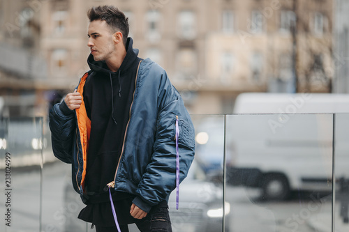 Fashionable man walk on the street near buildings. Wear blue jacket and all black. Winter, autumn outfit. Jacket with blouse and black sneakers.