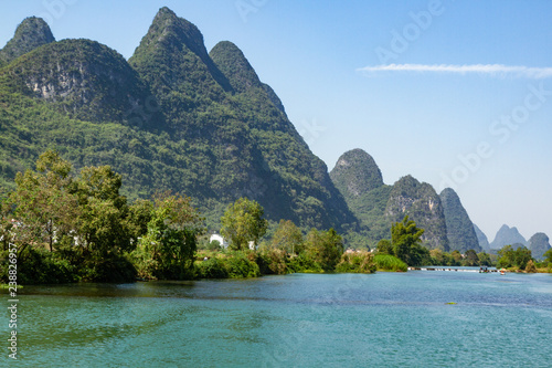 Color landscape photo of green limestone hills along the Yulong River in Yangshuo, Guilin, China. Partly cloudy blue sky, copy space.