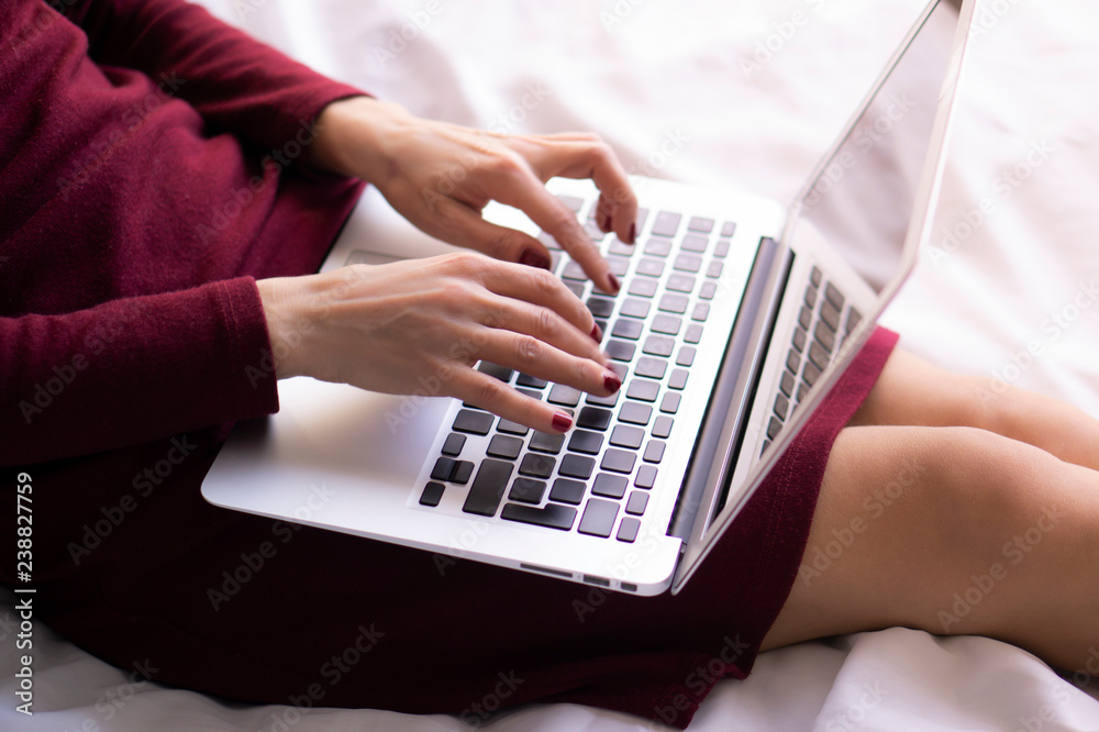Business woman is working with a laptop on her knees on the bed in the bedroom. Working at home. Business woman is working with a laptop on her knees on the bed in the bedroom. Working at home.