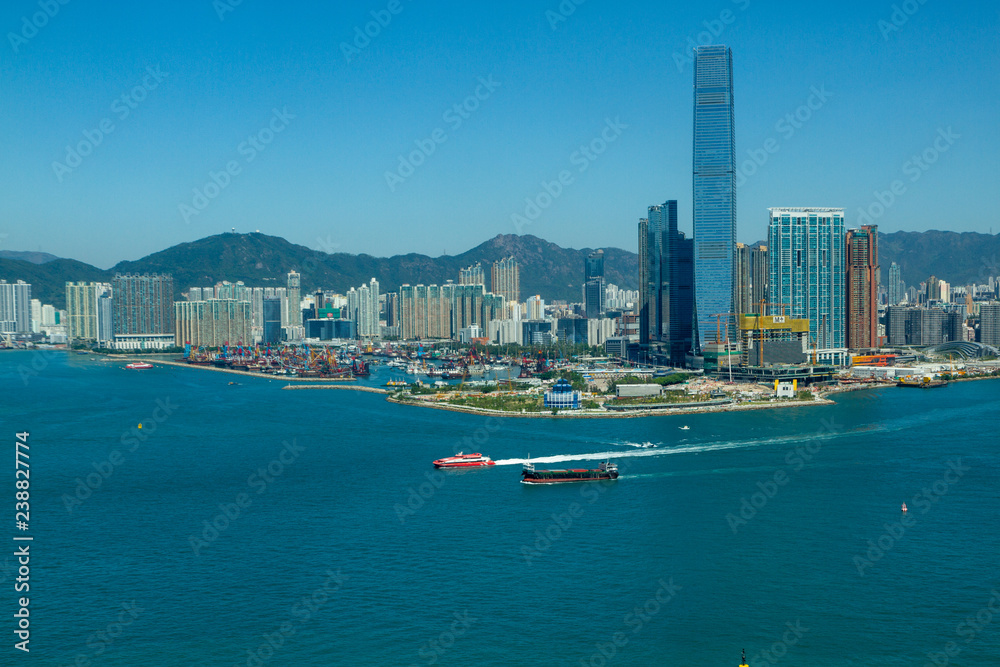 Hong Kong harbor during the day. Buildings on both sides of water. Boats visible on water.