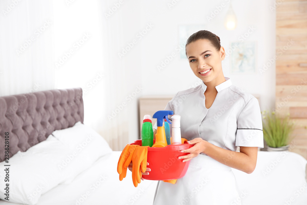 Young chambermaid with cleaning supplies in bedroom. Space for text Young chambermaid with cleaning supplies in bedroom. Space for text