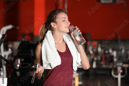 Beautiful young woman with towel and bottle of water in gym