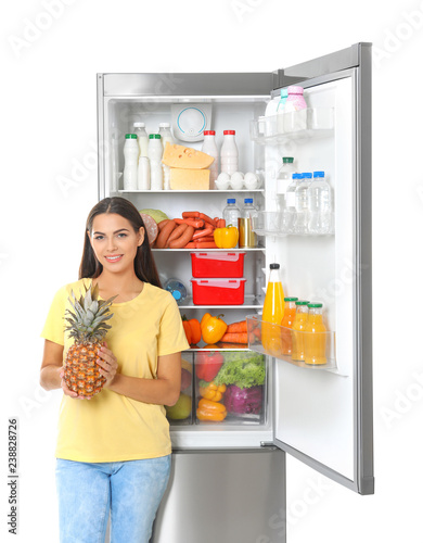 Young woman with pineapple near open refrigerator on white background
