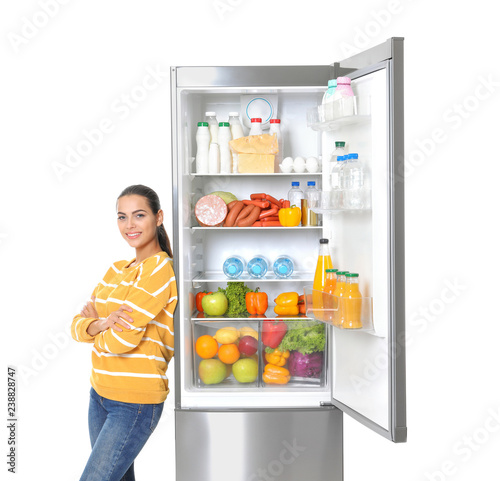 Young woman near open refrigerator on white background