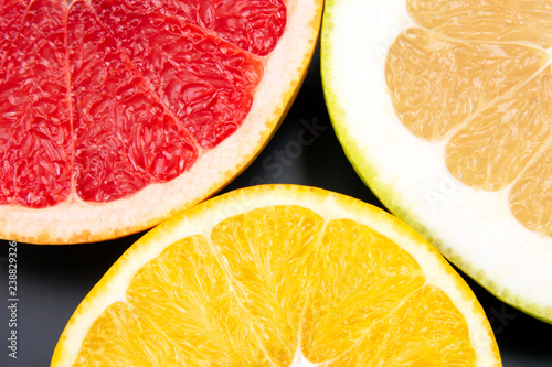 cut pieces of different citrus fruits on dark background