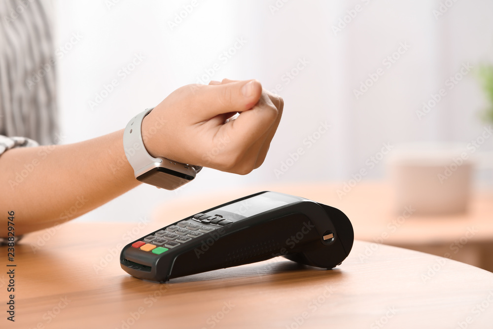 Fototapeta premium Woman using terminal for contactless payment with smart watch indoors