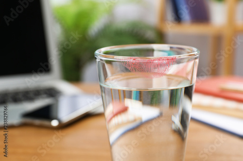Glass of water with lipstick mark at workplace, closeup