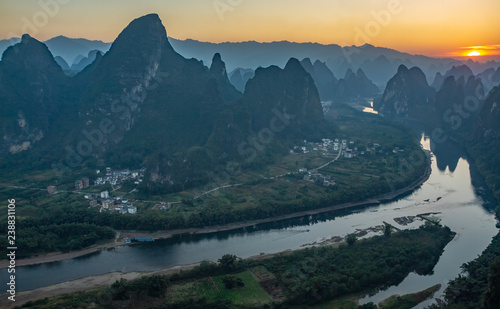 Sunrise over the Li River as seen from Xianggong mountain  Yangshuo  Guilin  China. Landscape is in silhouette with orange sun rising on upper right.