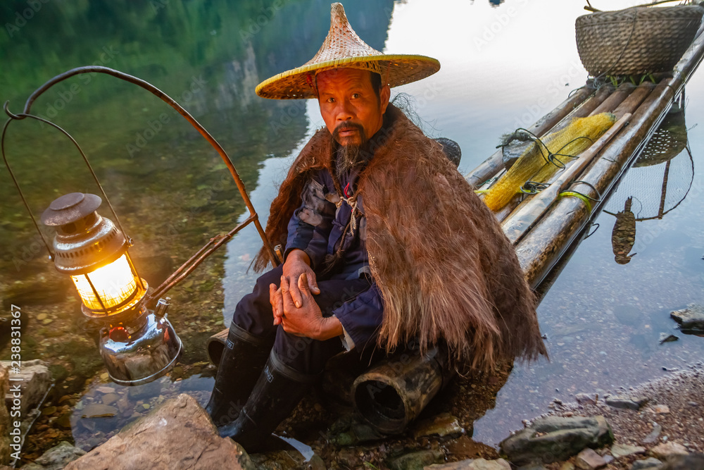 Chinese cormorant fisherman on raft in lake with a lighted lantern, a pipe,  and fishing gear in Guilin, China. Stock Photo
