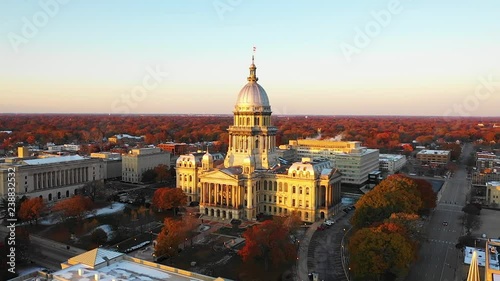 Stunning establishing aerial drone shot of the Illinois State Capitol Building in Springfield, Illinois, at dawn in November as the sun rises and fall leaves glow orange in the distance. photo