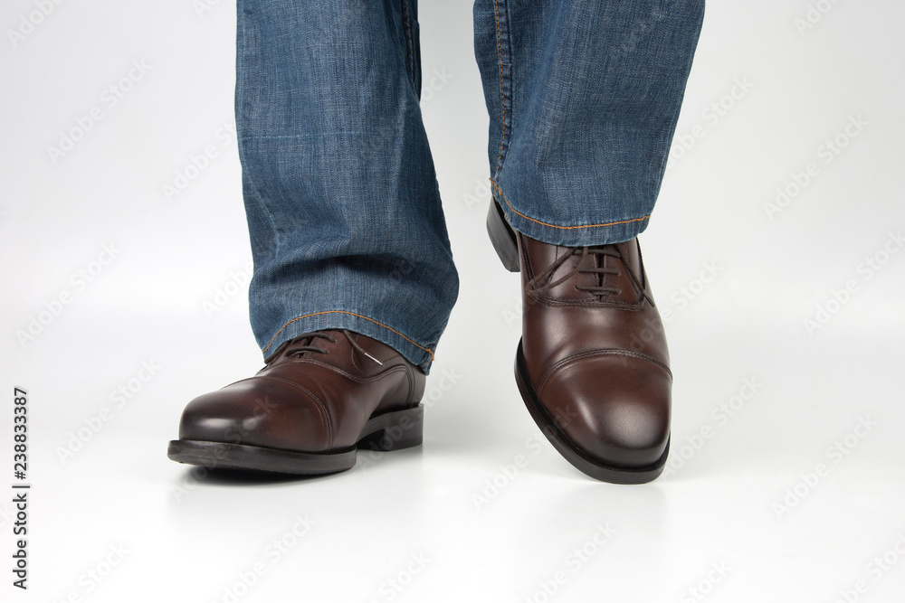 Male legs in jeans and brown classic shoes on white background