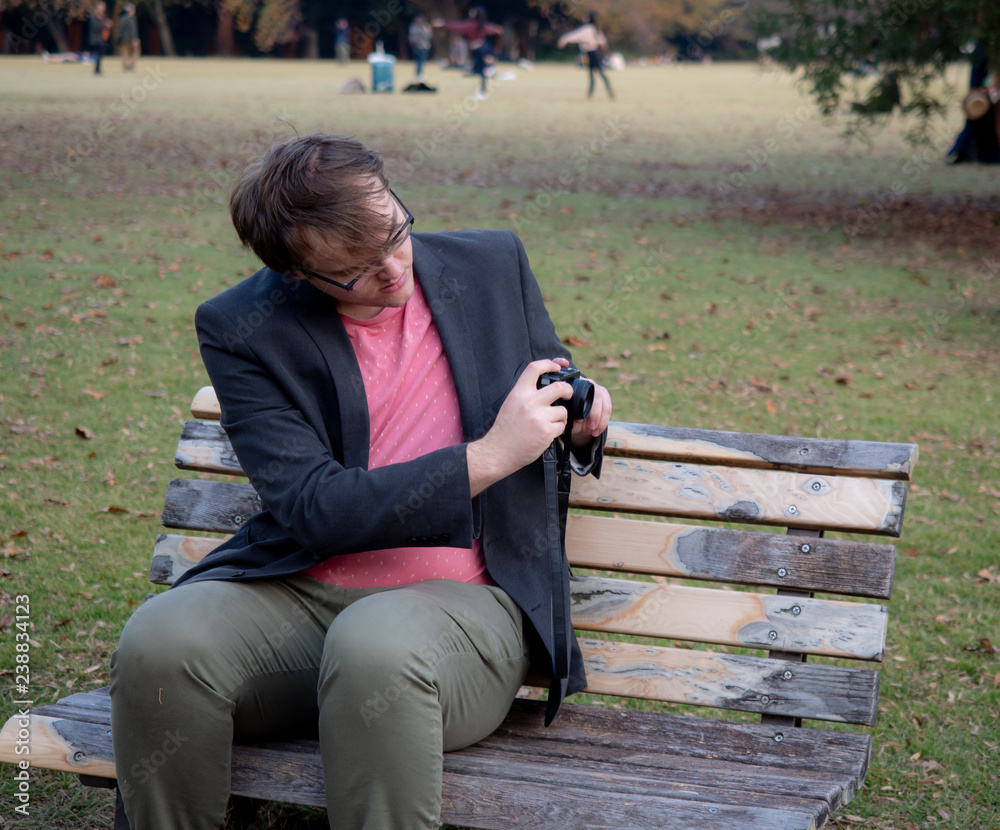 Fototapeta premium A man sat on a park bench taking pictures with his digital camera
