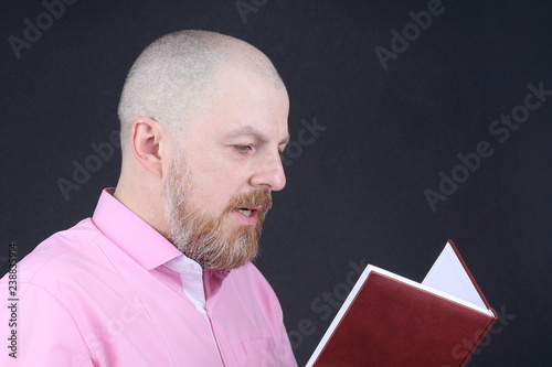 Bearded man in a pink shirt reading a book