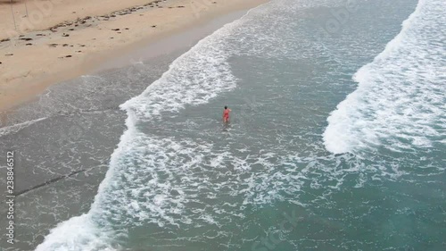 Aerial, zoom in, drone shot of a woman walking in the water, while waves hit the paradise beach, near Trincomalee city, on a cloudy day, in Gokanna, in the Eastern Province of Sri Lanka, Asia photo