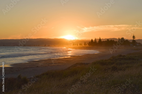 The bright sun sets on a quiet beach in Gisborne, New Zealand.